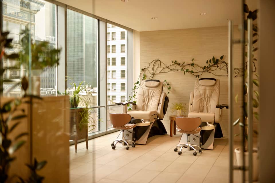 Nail salon with pedicure chairs, large windows with city views, and living plants as decoration