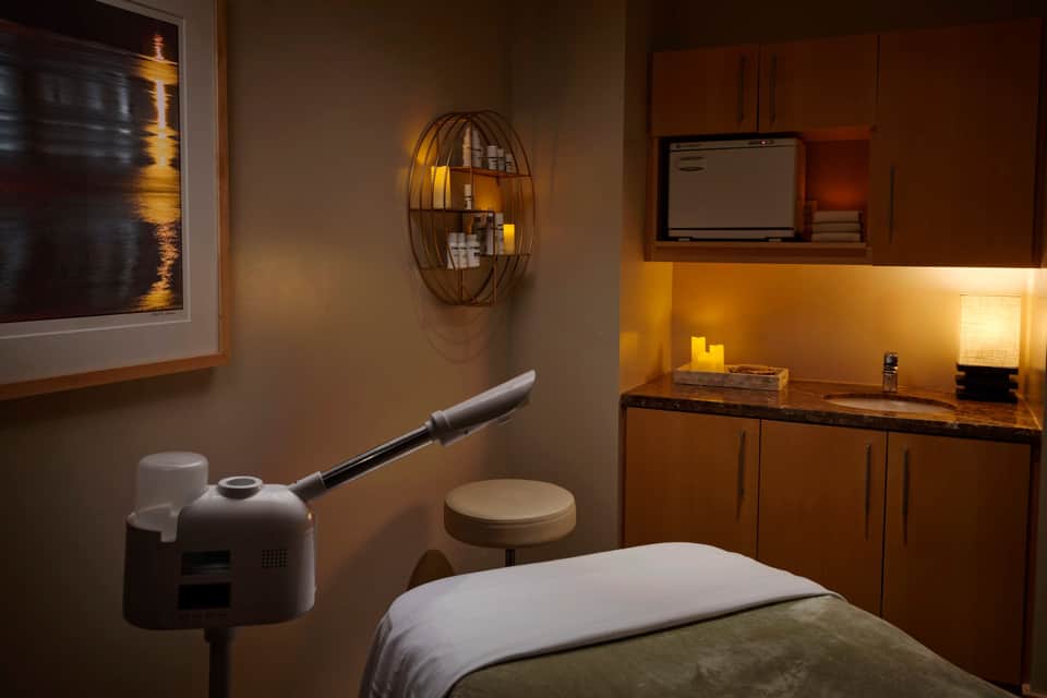Spa consultation room with treatment table, wood cabinetry, warm lighting, and modern amenities