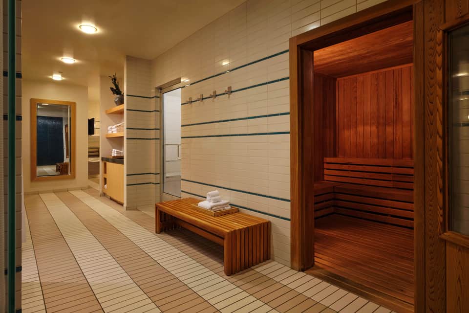 Luxury spa facility with sauna, shower area, wooden bench, and tiled flooring