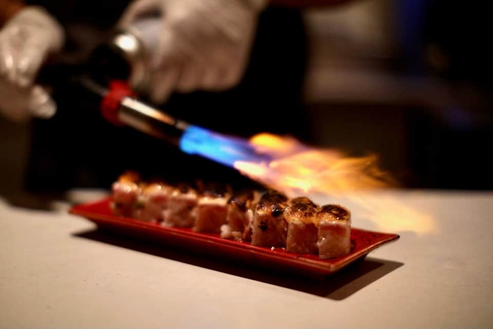 Chef using blowtorch to finish seared scallops on red plate during fine dining preparation