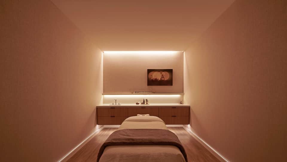 Minimalist massage room with warm lighting, wooden vanity, and comfortable massage bed