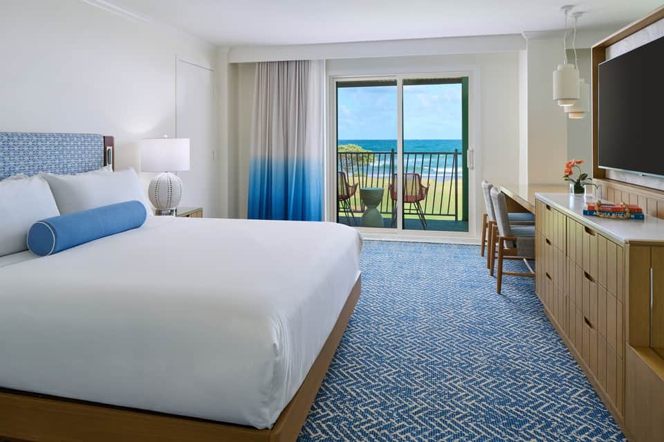 Modern hotel bedroom with ocean balcony view, blue ombre curtains, and contemporary furnishings