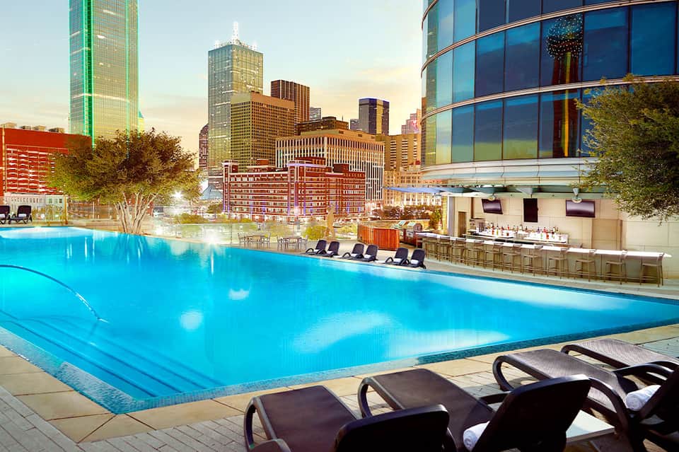Urban rooftop pool at dusk with city skyline and lounge chairs