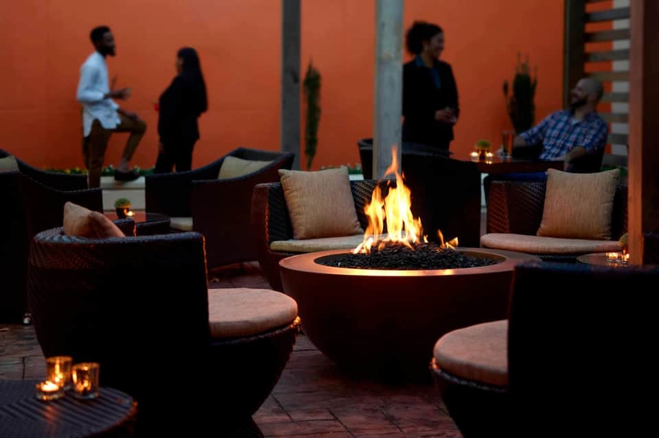 Outdoor fire pit lounge area with upholstered seating and warm lighting at evening with guests mingling