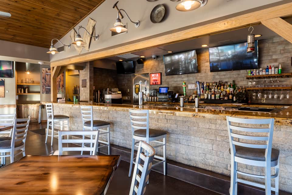 Modern bar interior with stone accent wall, wooden ceiling, white bar stools and flat-screen TVs