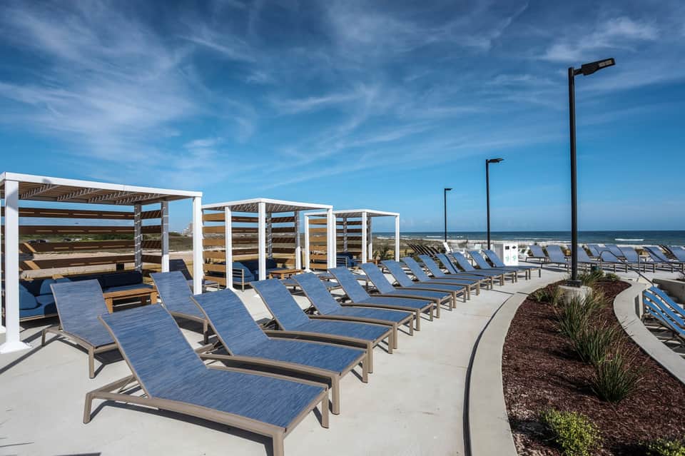 Oceanfront beach deck with blue lounge chairs, white shade structures, and panoramic sea views