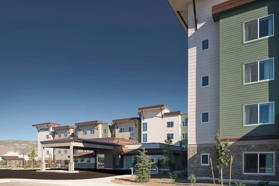 Multi-story residential complex with mixed pastel siding, stone base, and covered entrance under clear blue sky