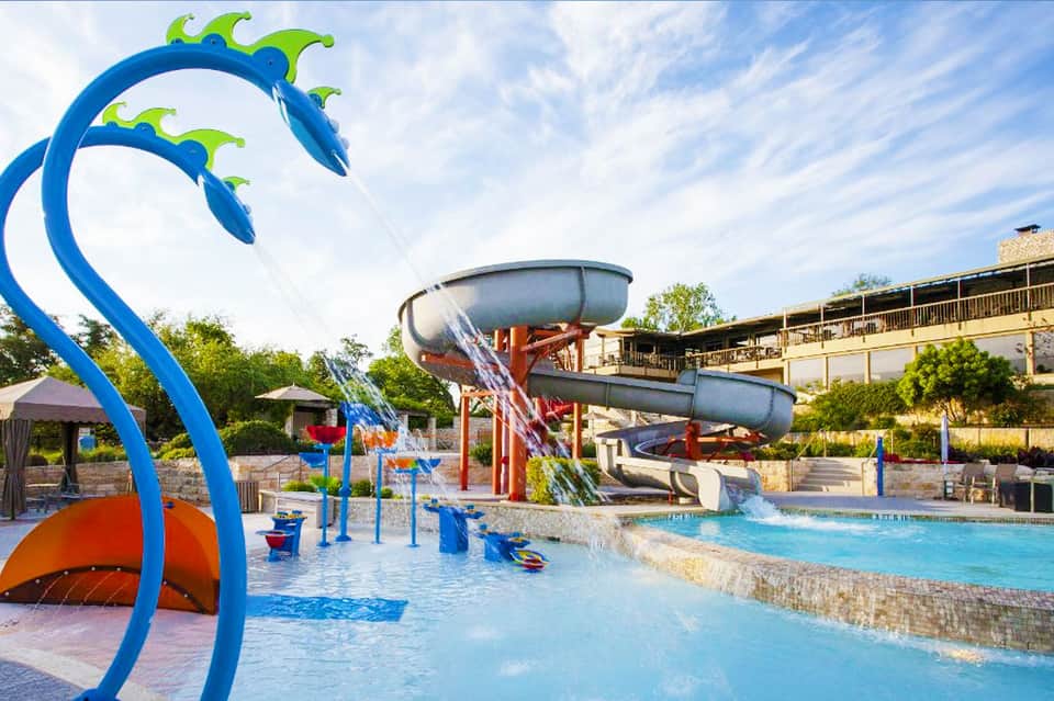 Colorful water park with blue slide structures, splash pad, and turquoise pool under clear sky