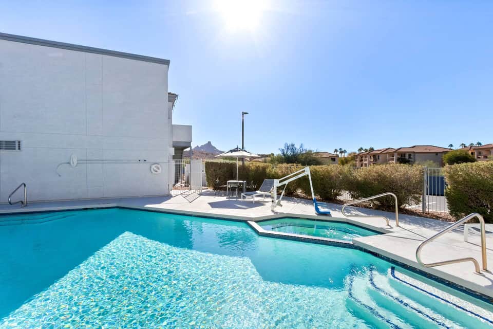Outdoor pool and hot tub with desert landscape and mountain views under clear sky