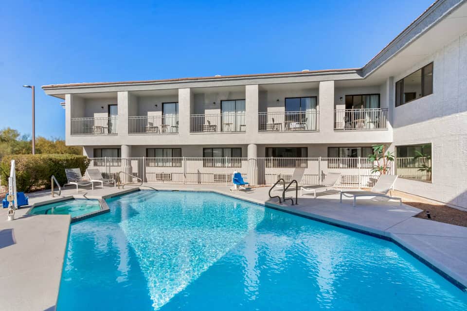 Resort exterior with two-story white building, multiple balconies, and sparkling blue pool