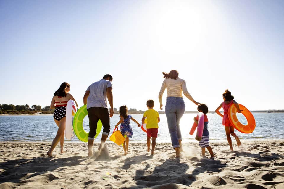 Family with children and colorful floats playing together on sandy beach near water