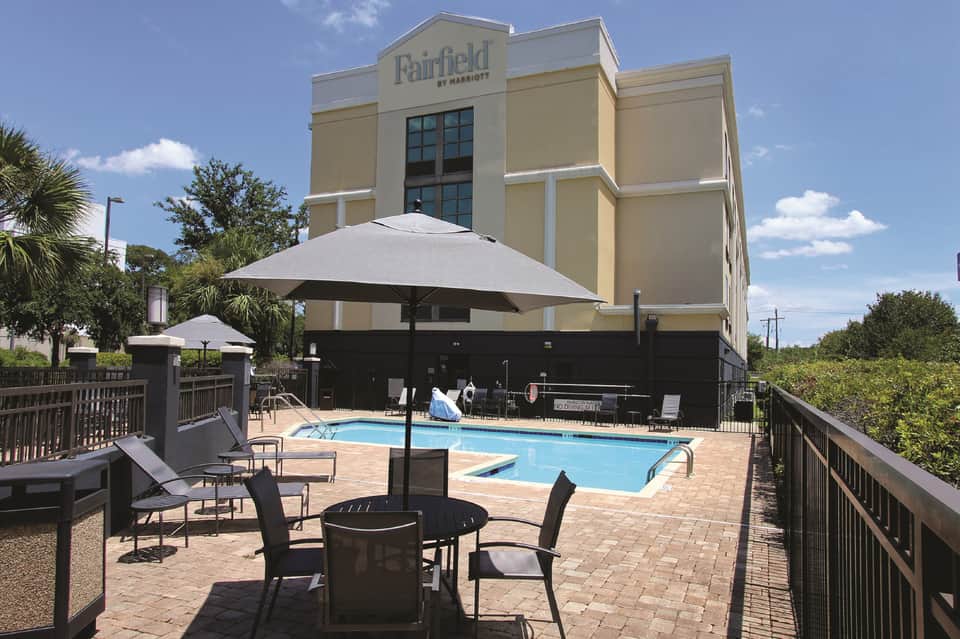 Fairfield by Marriott exterior with poolside seating, umbrellas, and palm trees in sunny setting