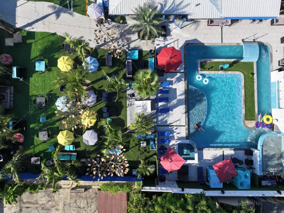 Aerial view of resort with turquoise pool, lush landscaping, colorful umbrellas, and lounge areas