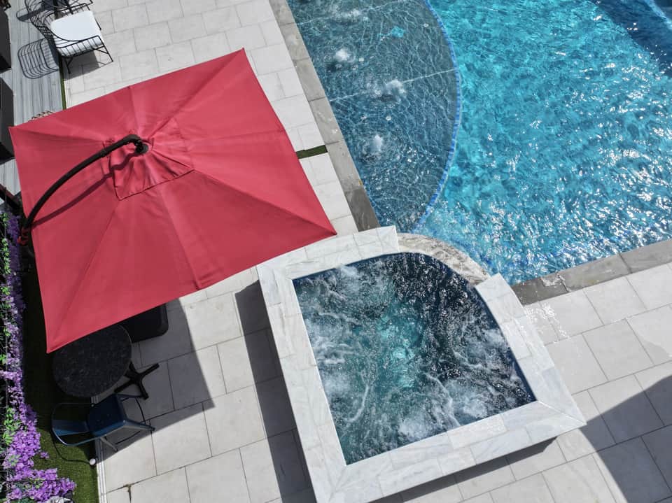 Red cantilever umbrella beside rectangular pool with white patio decking and spa jets