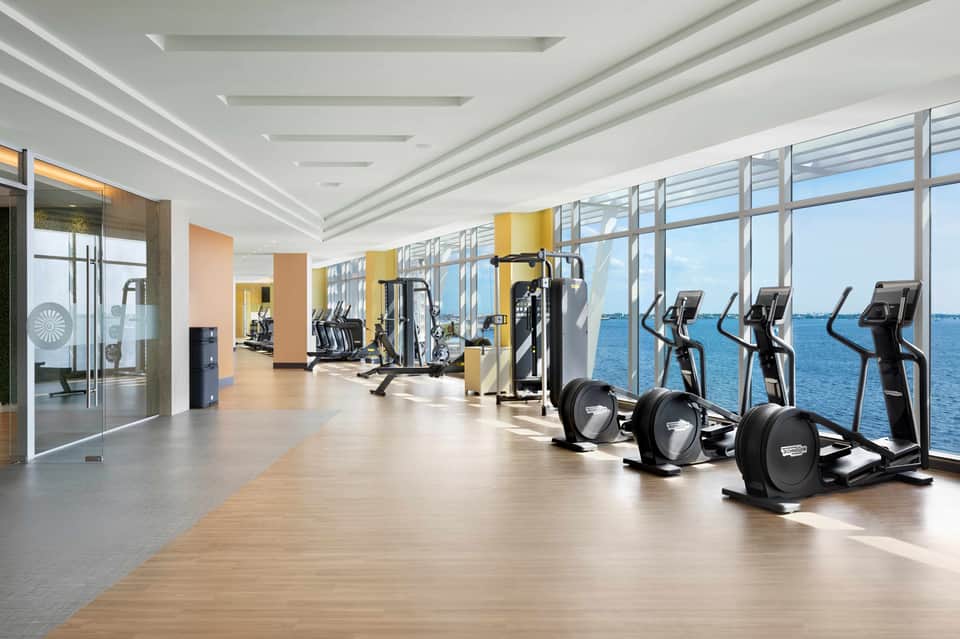 Spacious gym with ocean view windows, elliptical machines, and strength training equipment