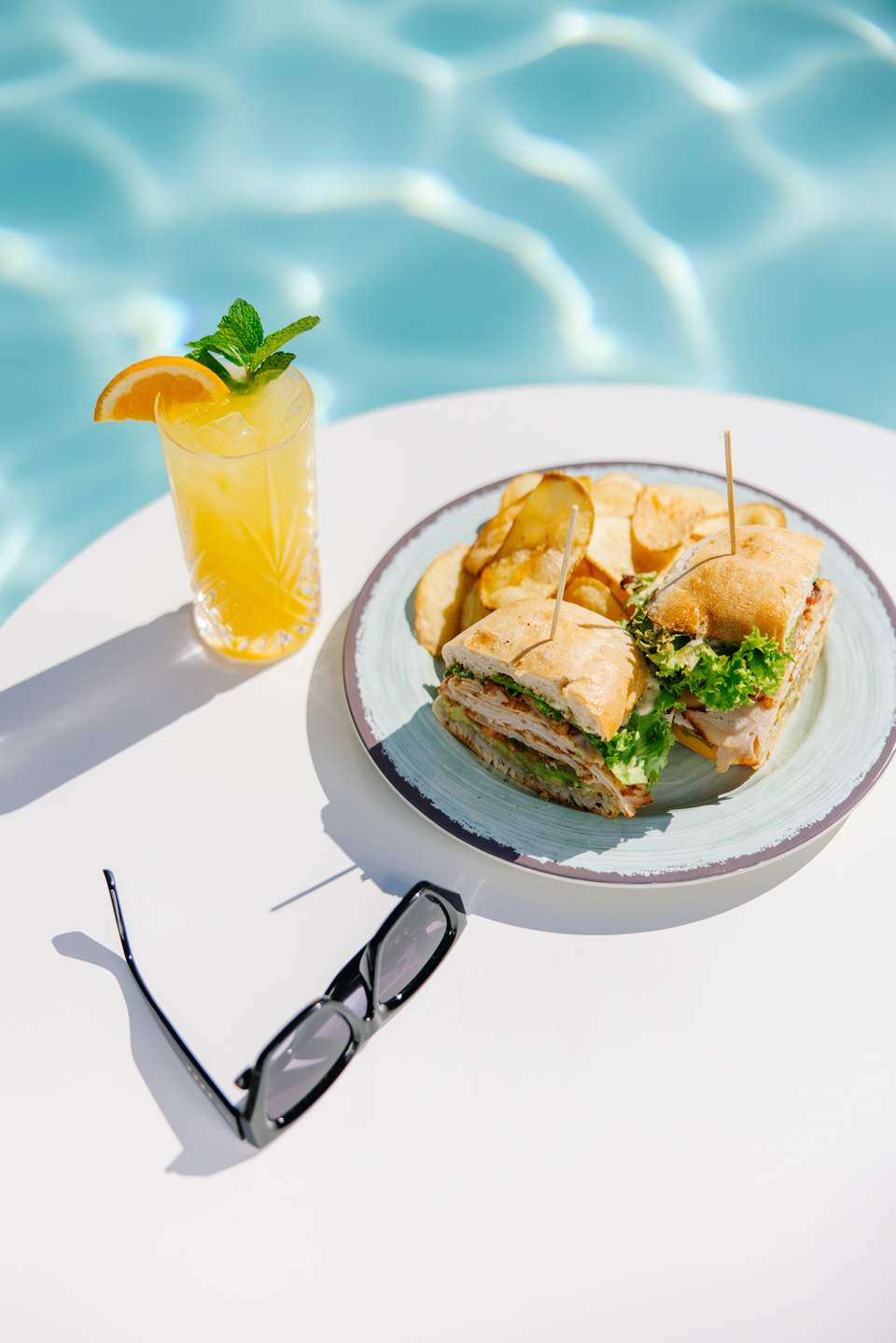 Poolside lunch setting with tropical cocktail, sandwich, and fries by swimming pool
