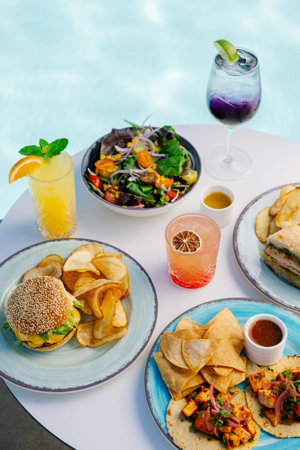 Resort poolside table with multiple gourmet dishes, fresh salad, and colorful beverages