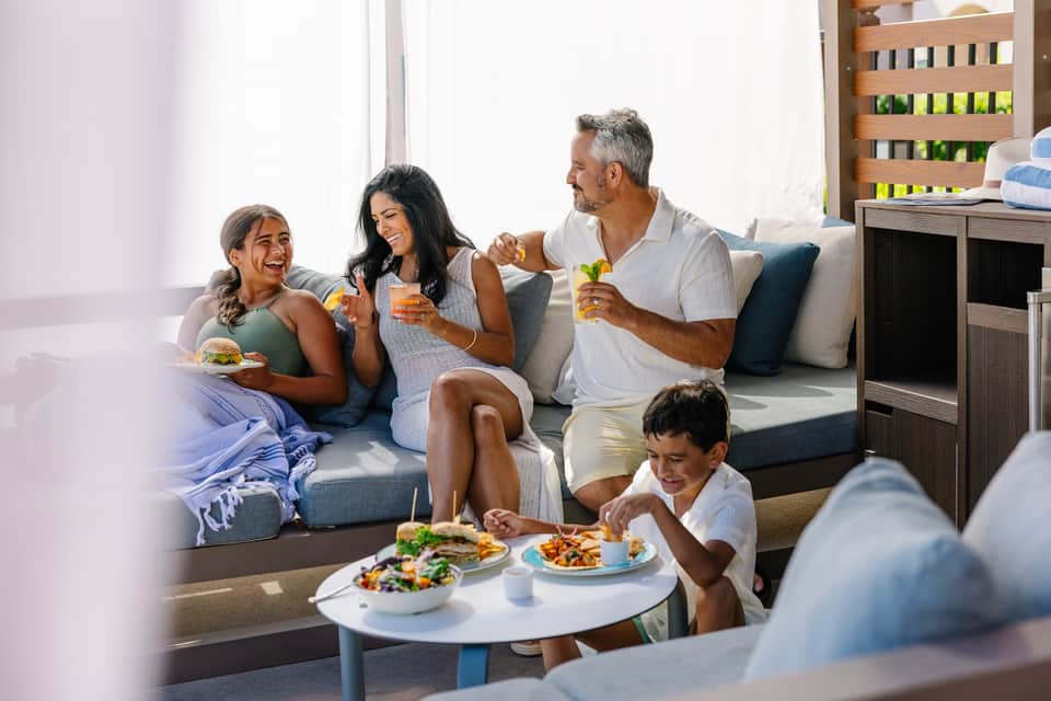 Family of four enjoying beverages and food together on a gray couch in a bright living room