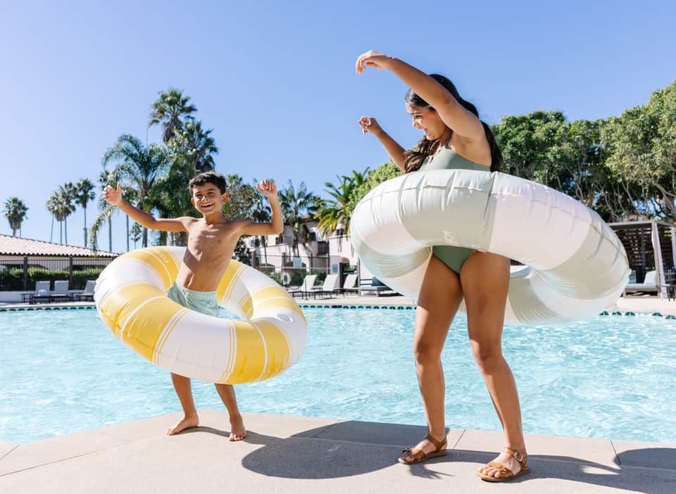 Woman and boy playing with inflatable pool floats in a resort pool with palm trees