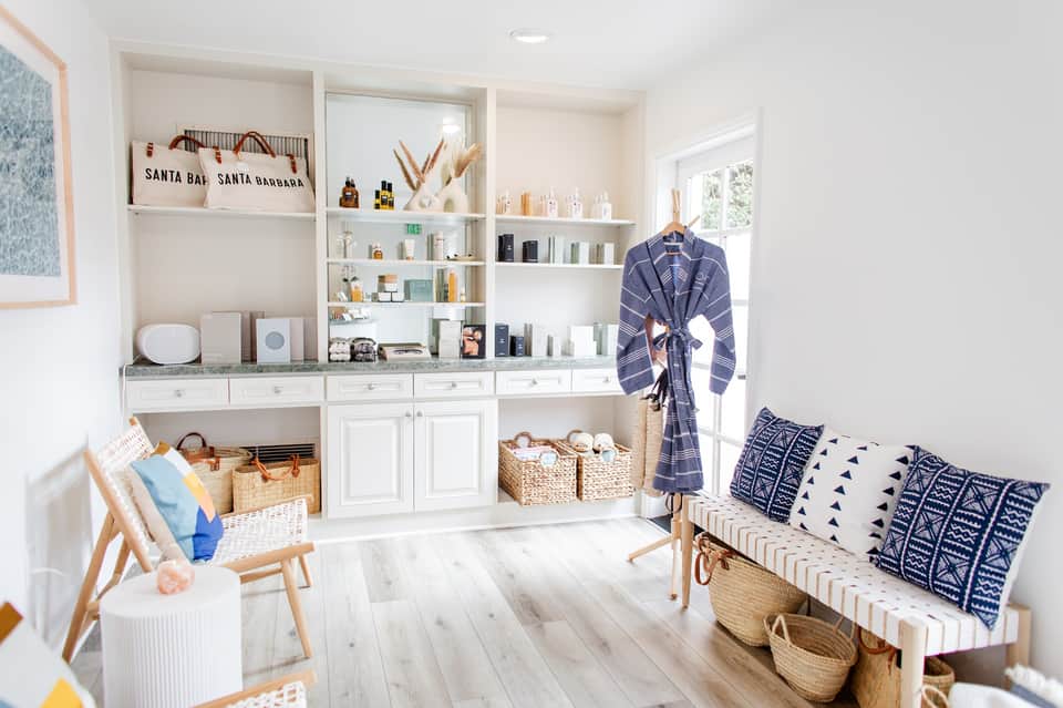 Bright retail spa boutique with white shelving, products, hanging robe, and striped bench seating