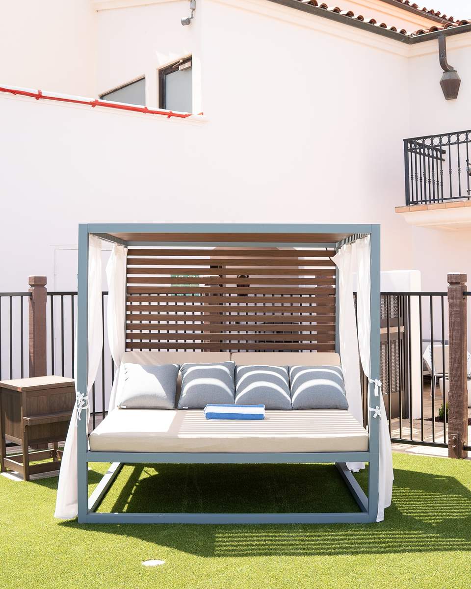 Elegant canopy daybed with striped blue and white pillows on manicured lawn with building backdrop