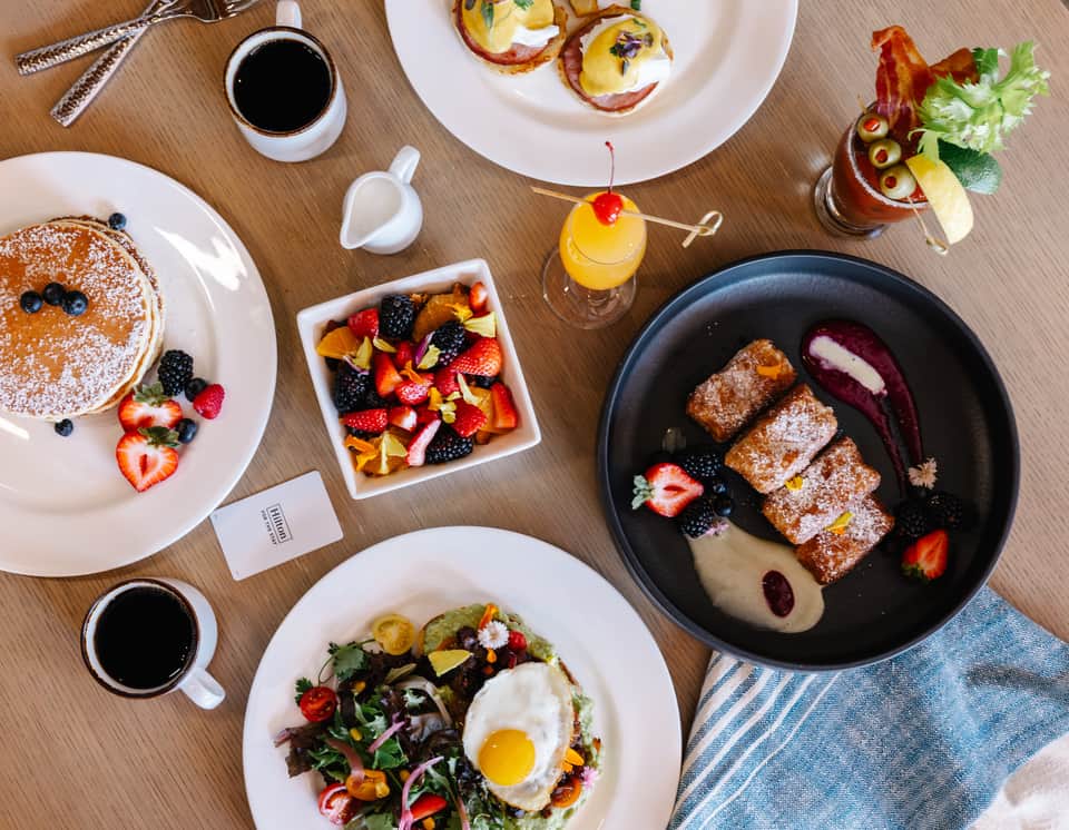 Breakfast spread featuring pancakes, pastries, fresh fruit, and beverages on wood table
