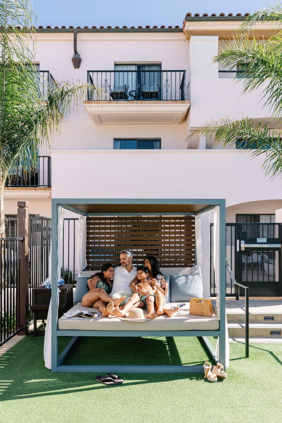 Father and children relaxing in modern canopy daybed on lawn beside resort building