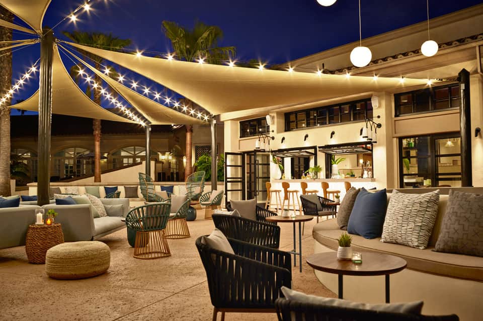 Elegant outdoor patio at night with illuminated sail shade, lounge seating, bar counter, and string lights