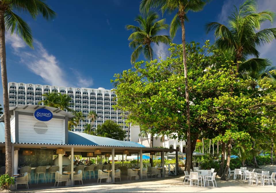 Beachfront restaurant pavilion with Royal Sonesta hotel tower, palm trees, and ocean backdrop