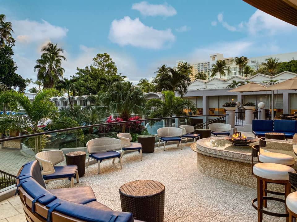 Upscale resort terrace with lounge seating, fire pit, and tropical garden overlooking pool area