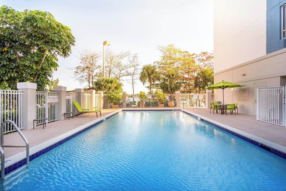 Resort swimming pool with white fencing, tropical landscaping, and lounging areas