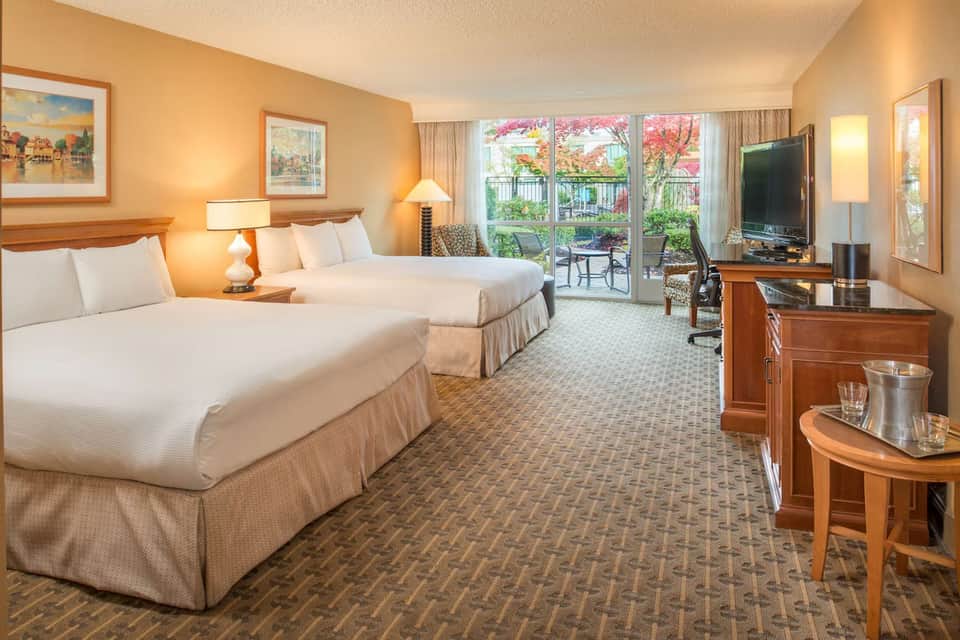 Hotel guest room with two queen beds, balcony access, flat-screen TV, and warm lighting