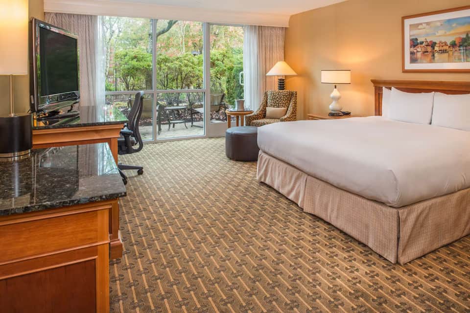 Suite with king bed, work area, balcony doors with tree views, and contemporary furnishings