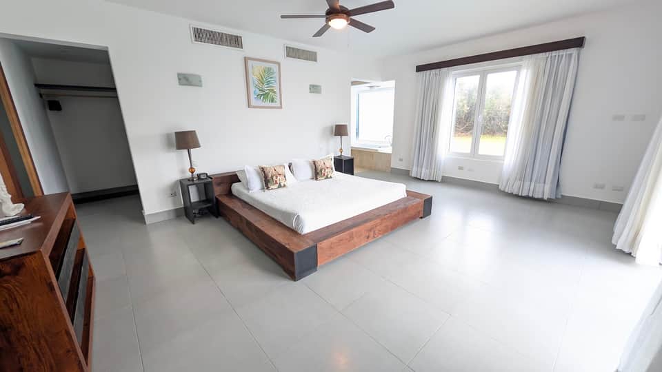 Spacious master bedroom with wooden platform bed, white tile floor, and garden views