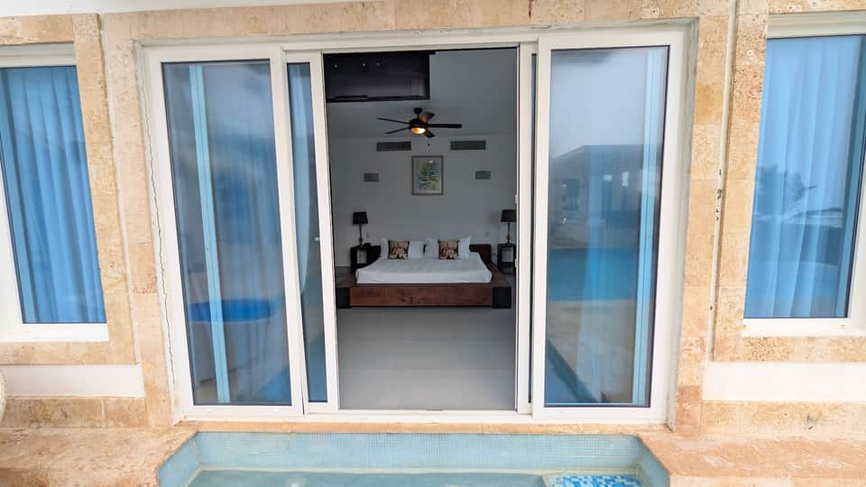 Beachfront bedroom with sliding glass doors opening to ocean views and small pool