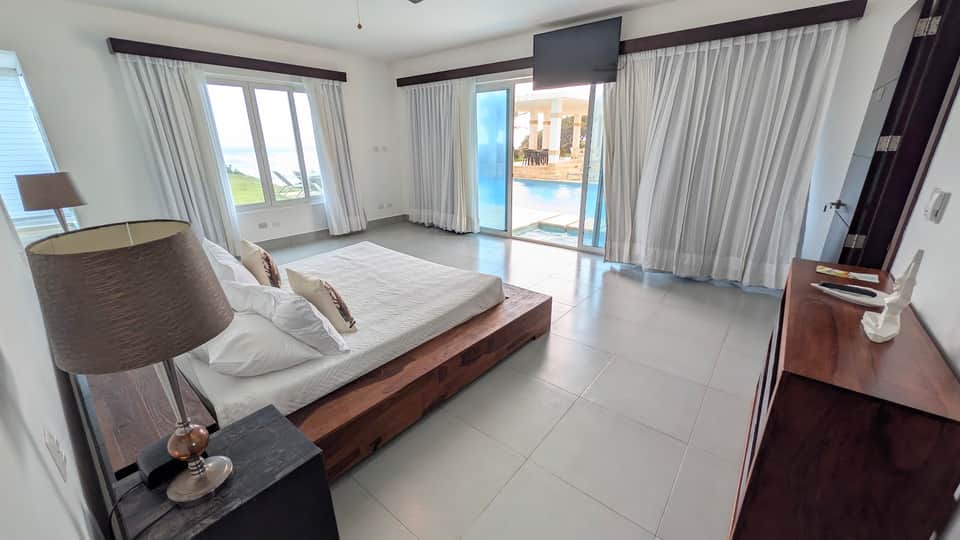 Modern waterfront bedroom with wooden bed, multiple glass doors, and water views