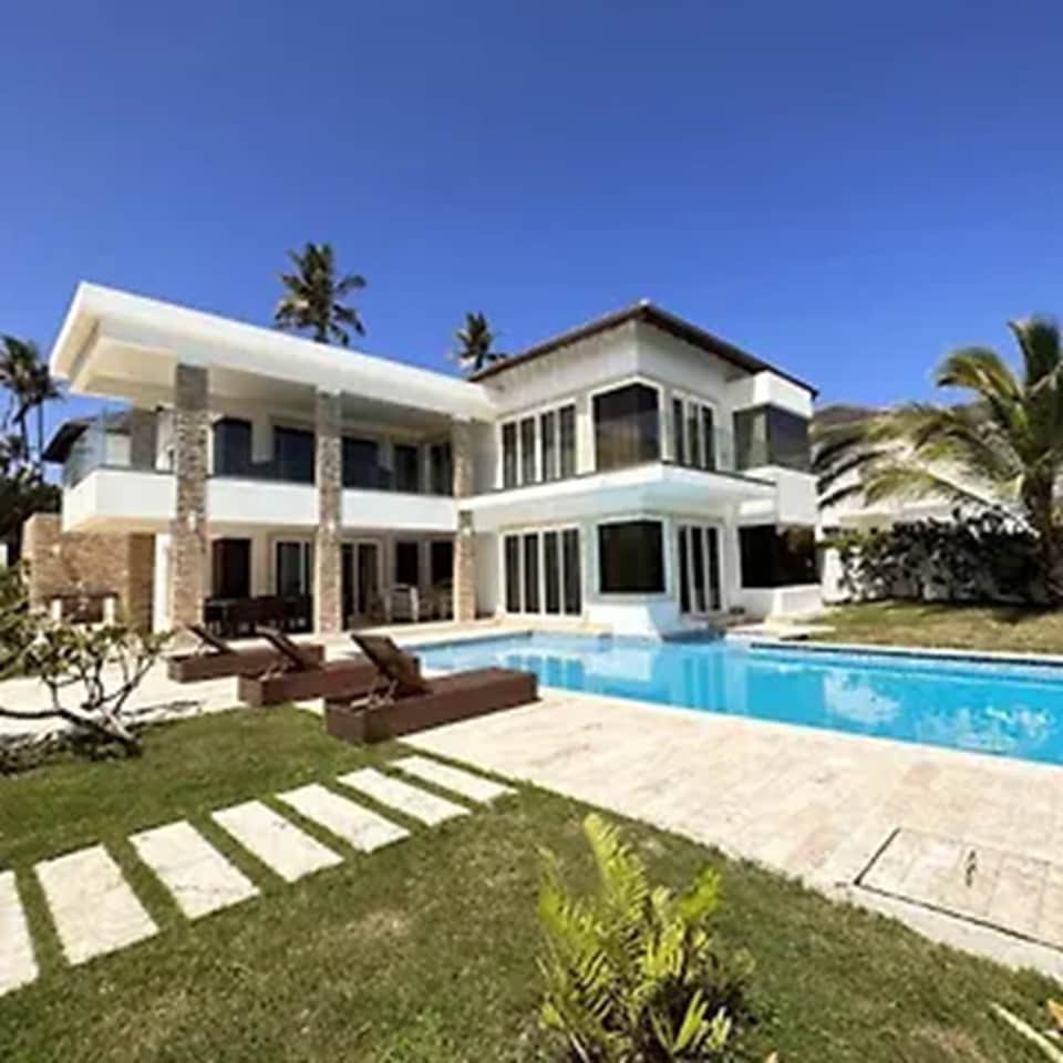 Modern two-story white villa with swimming pool, palm trees, and manicured lawn in tropical setting