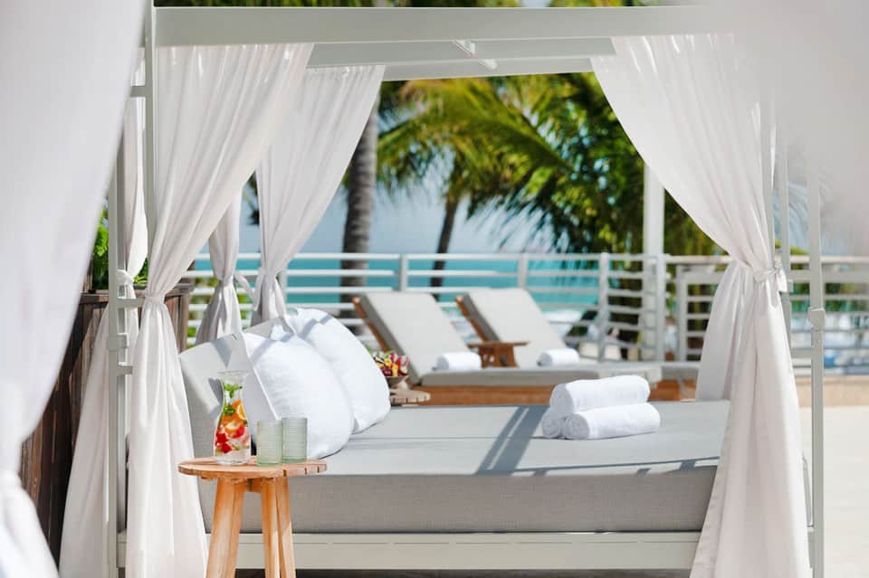 Luxury cabana with flowing white curtains overlooking turquoise water and lounge chairs with white pillows
