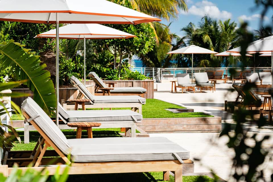 Tropical resort deck with wooden lounge chairs, white umbrellas, and ocean view