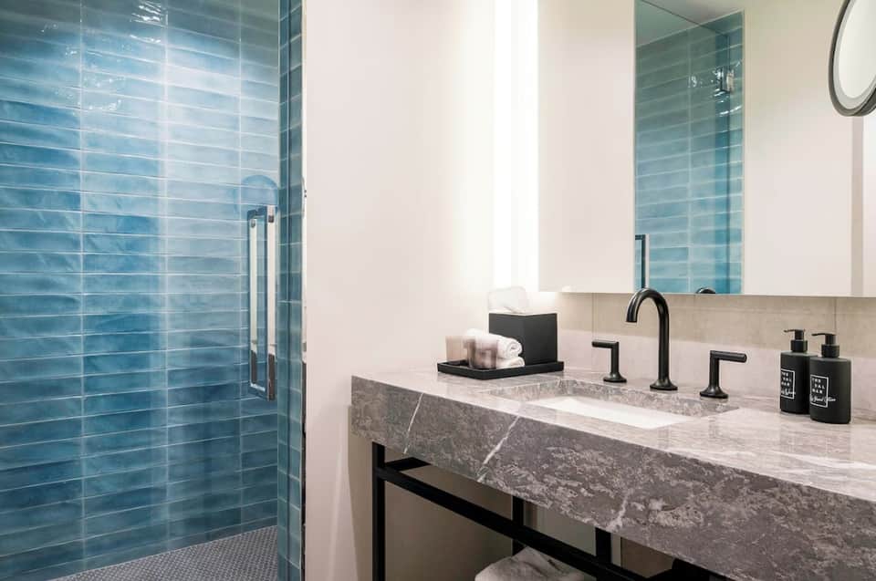 Luxury bathroom with blue tile shower, marble countertop, black fixtures, and modern circular mirror