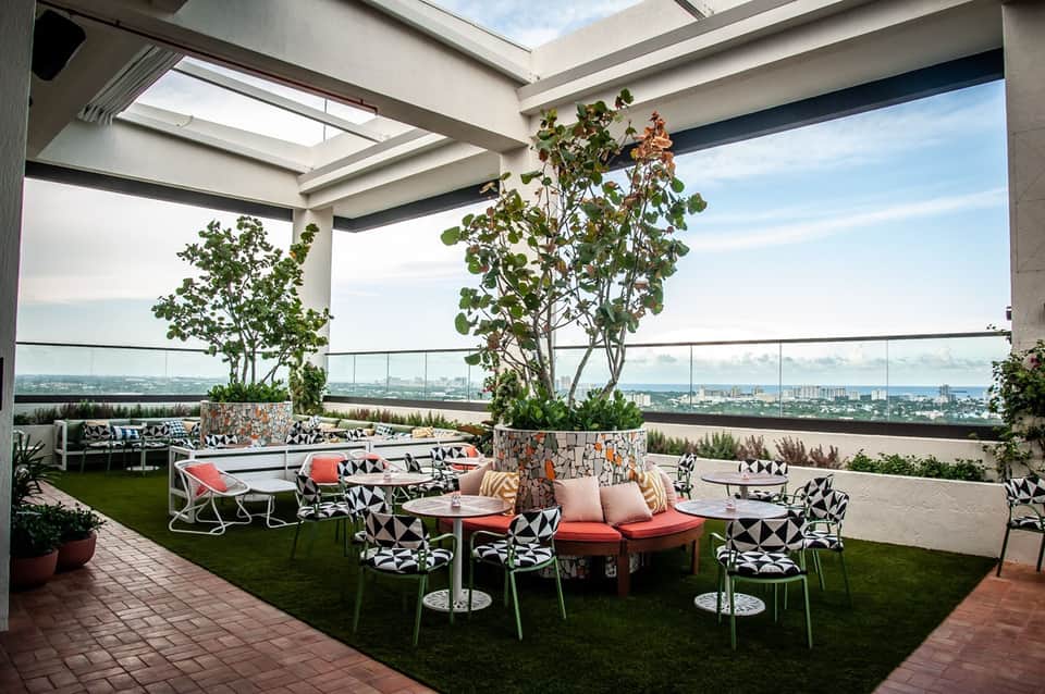 Rooftop terrace with modern seating, potted plants, glass railings, and expansive city skyline views