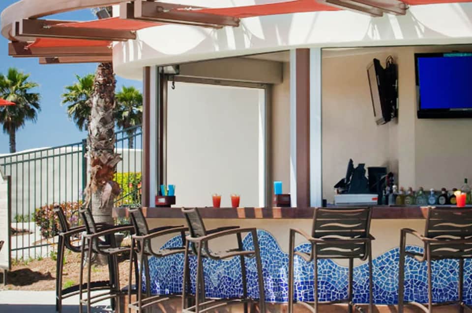 Upscale poolside bar with blue patterned seating, orange shade structure, and ocean views with palm trees