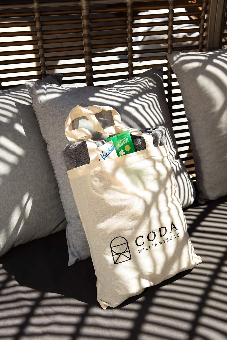 CODA Williamsburg branded canvas tote bag on lounge chair with striped shade pattern