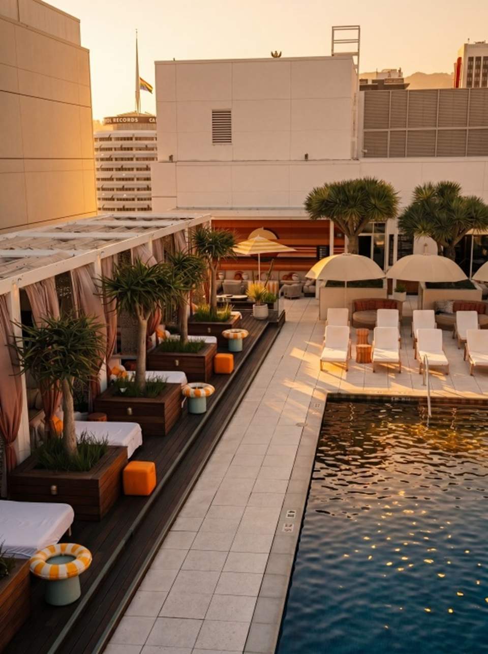 Resort pool deck at sunset with cabanas, loungers, umbrellas, and landscaping beside water