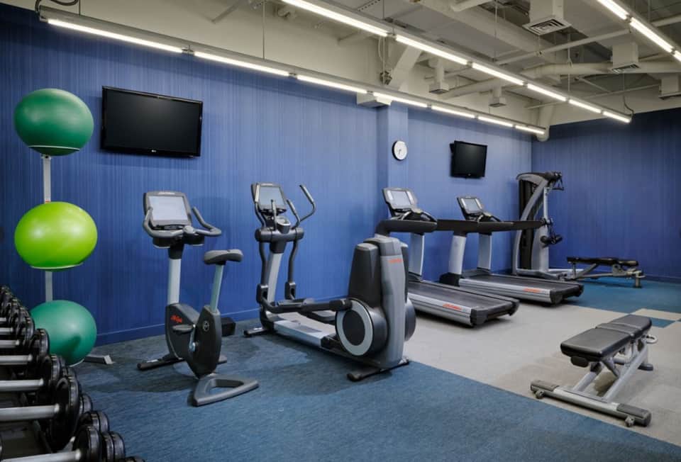 Fitness center with exercise bikes, treadmills, stability balls, and TV monitors on blue walls
