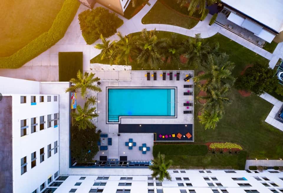 Aerial view of resort pool surrounded by landscaping, seating areas, and modern white buildings