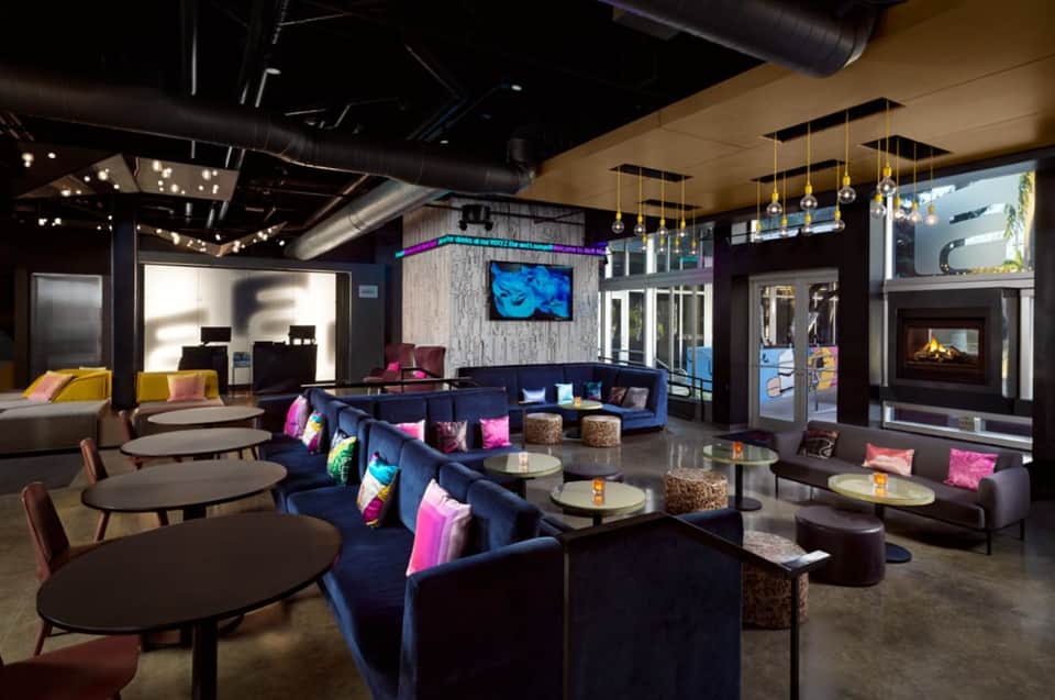 Modern hotel lounge with blue sectional seating, colorful pillows, pendant lighting, and fireplace