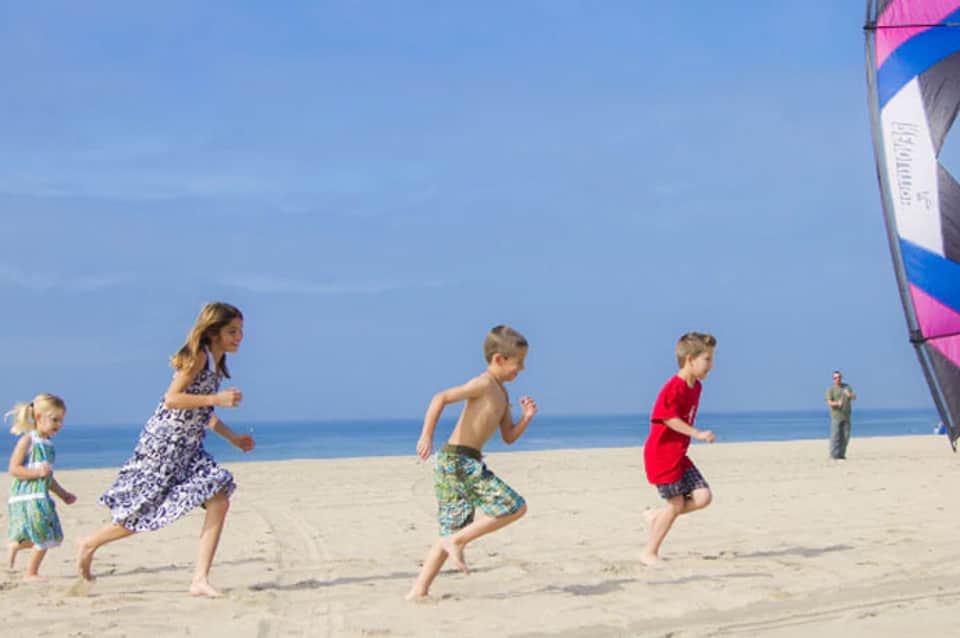Children running on sandy beach with colorful kite in background