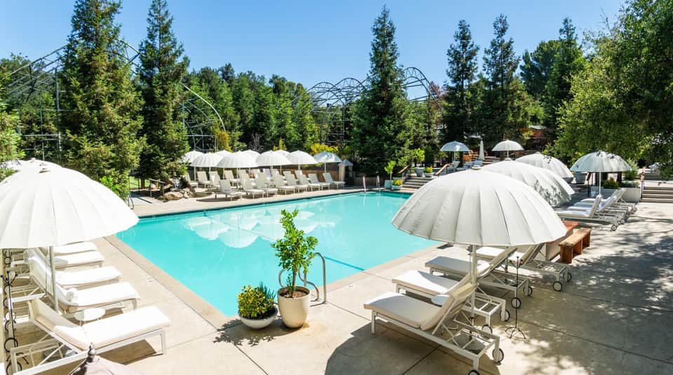 Outdoor resort pool with surrounding white umbrellas, lounge chairs, and forested landscape