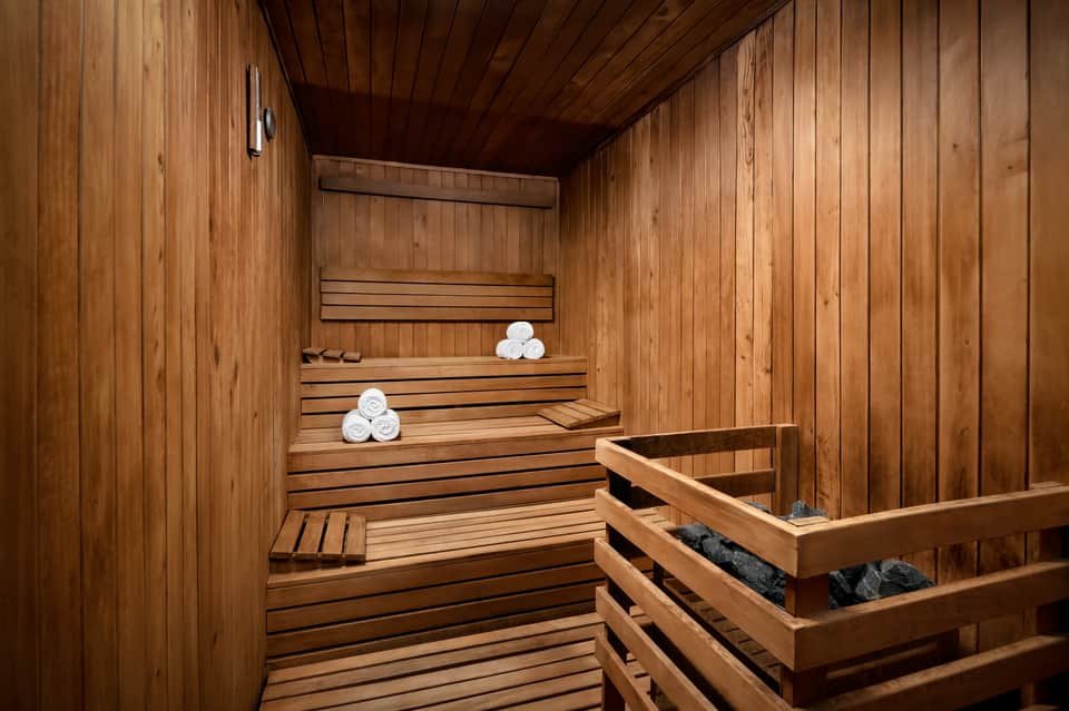 Traditional wooden sauna interior with tiered benches, white towels, and black heating stones